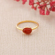 14k Gold filled ring with a red Carnelian stone on a beige fabric background with red flowers.