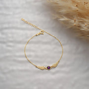 14k Gold angel wings bracelet with a Ruby gemstone on a soft white background