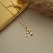 14k Gold heart-shaped necklace with a cross on a beige background