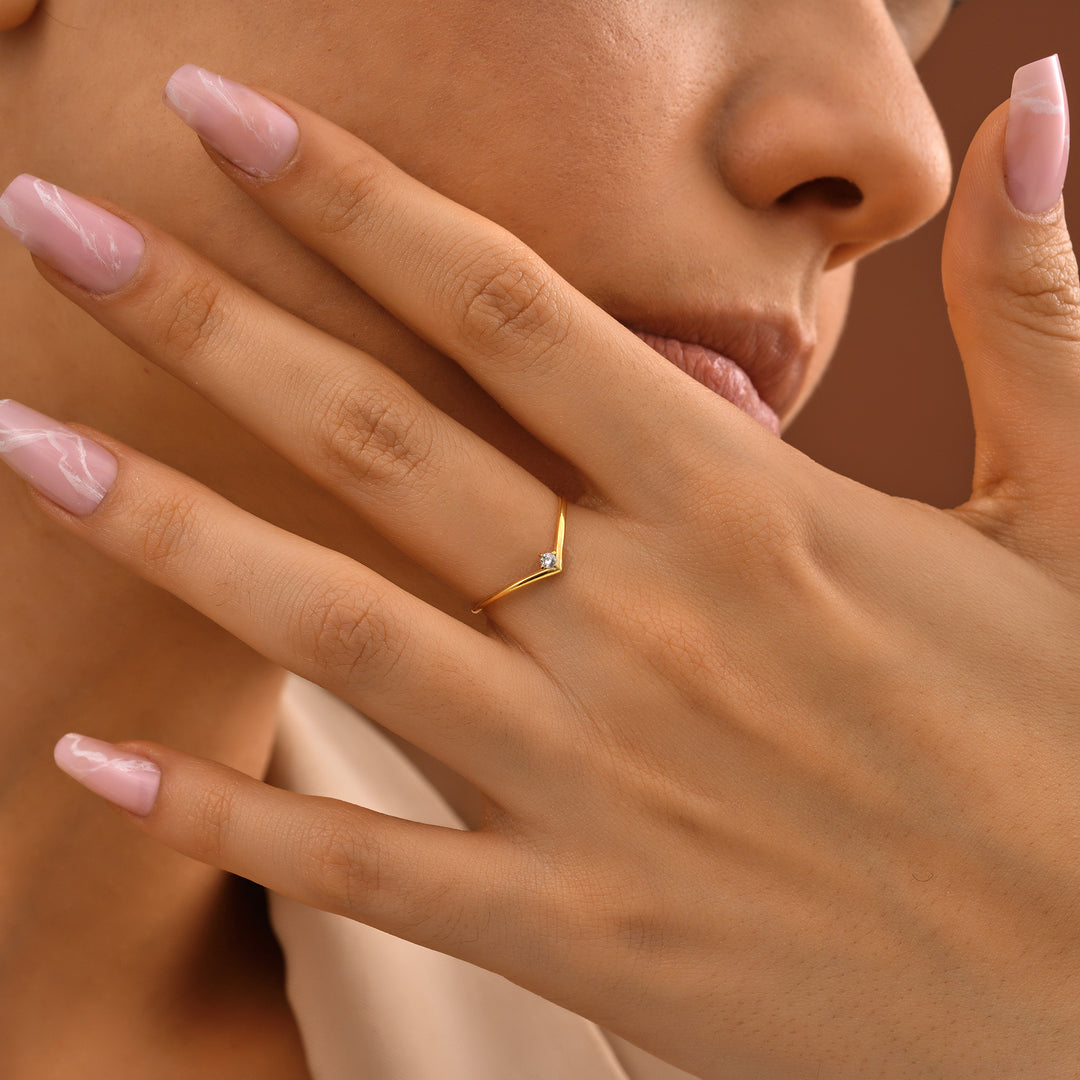 Diamond Chevron Ring Close-up of a hand wearing a gold ring with a diamond on a brown background