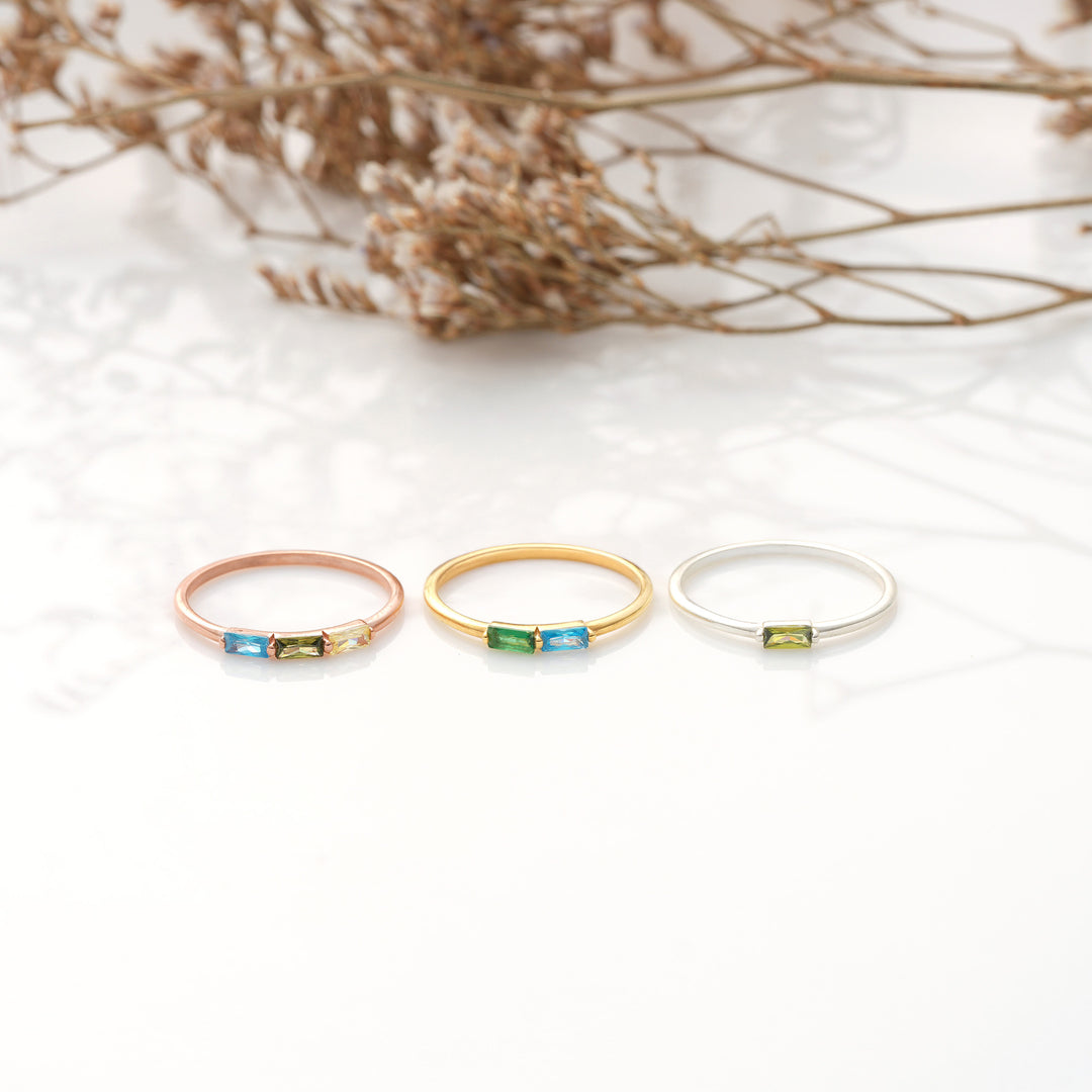 Three rings in gold, rose gold, and silver with gemstones on a white background.
