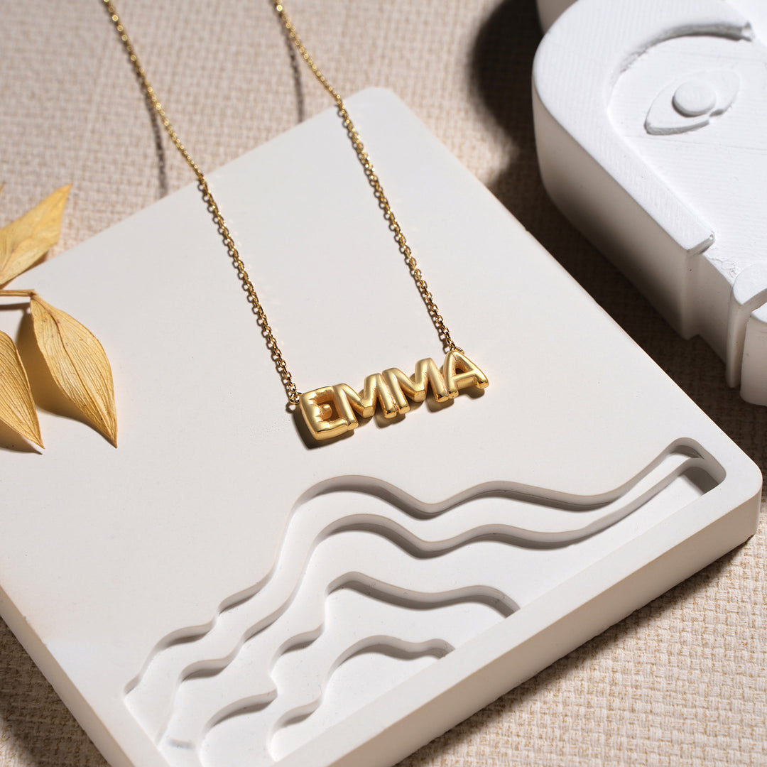 Gold necklace with 'EMMA' pendant on a white jewelry box
