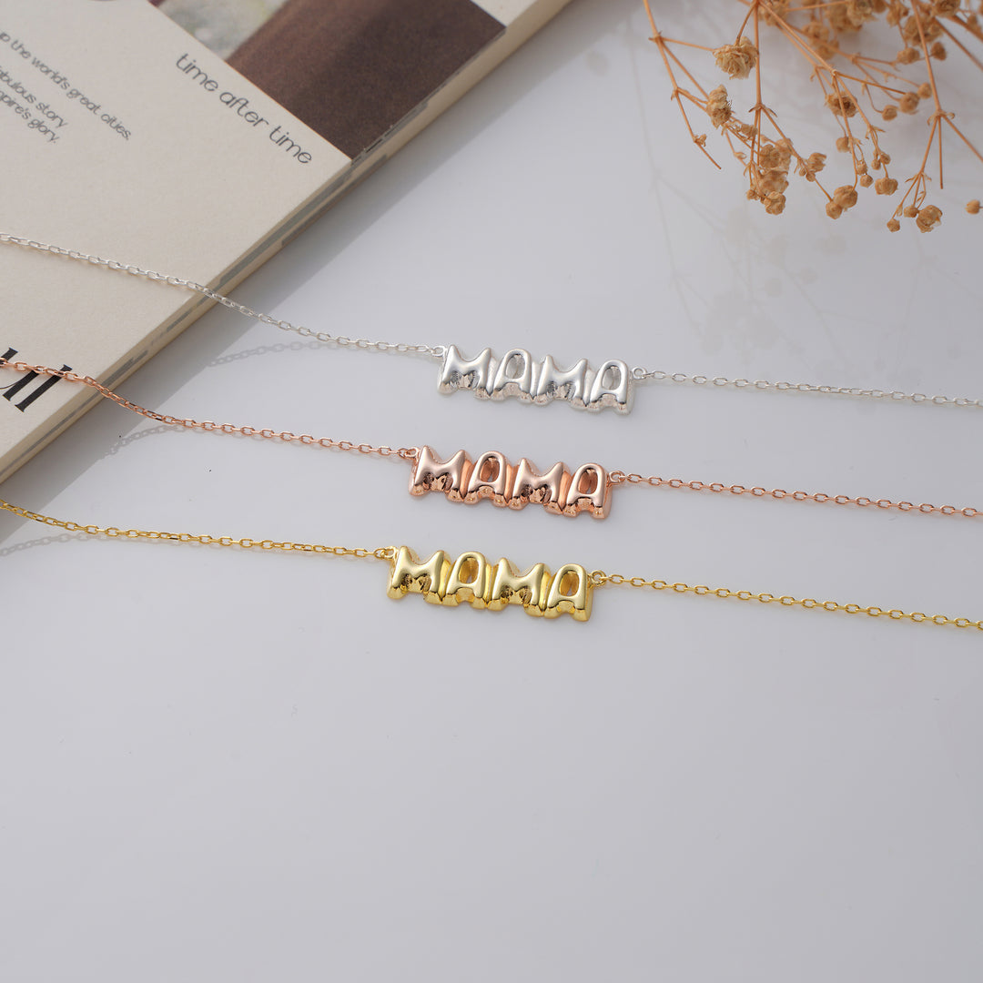 Three gold necklaces with 'MAMA' on a light surface.