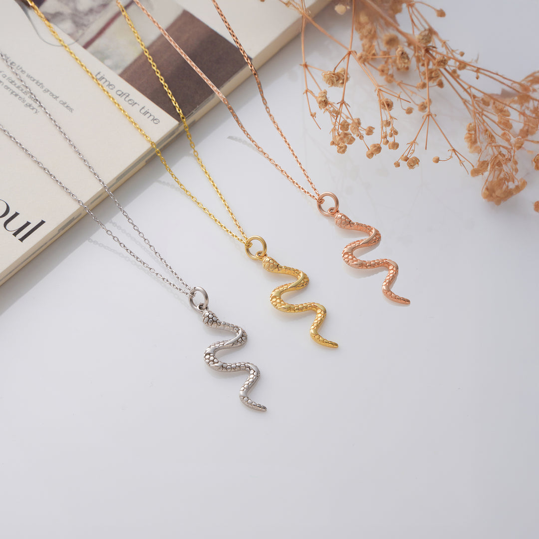 Three necklaces with unique pendants on a light surface with dried flowers.