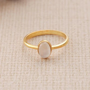 14k Gold filled oval ring with a white moonstone on a beige fabric background