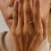 Close-up of a hand wearing a 14k gold filled ovel birthstone cz ring with a green emerald gemstone, held near the face.