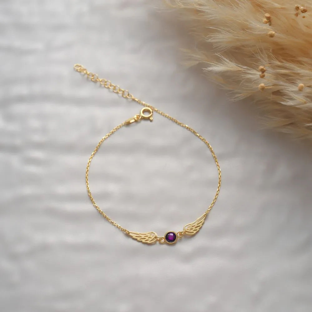 14k Gold angel wings bracelet with a Ruby gemstone on a soft white background
