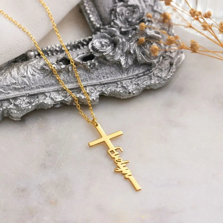 14k Gold cross necklace with name on a decorative silver dish.