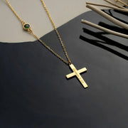 14k Gold necklace with an engraved cross pendant  and emerald birthstone on a dark surface