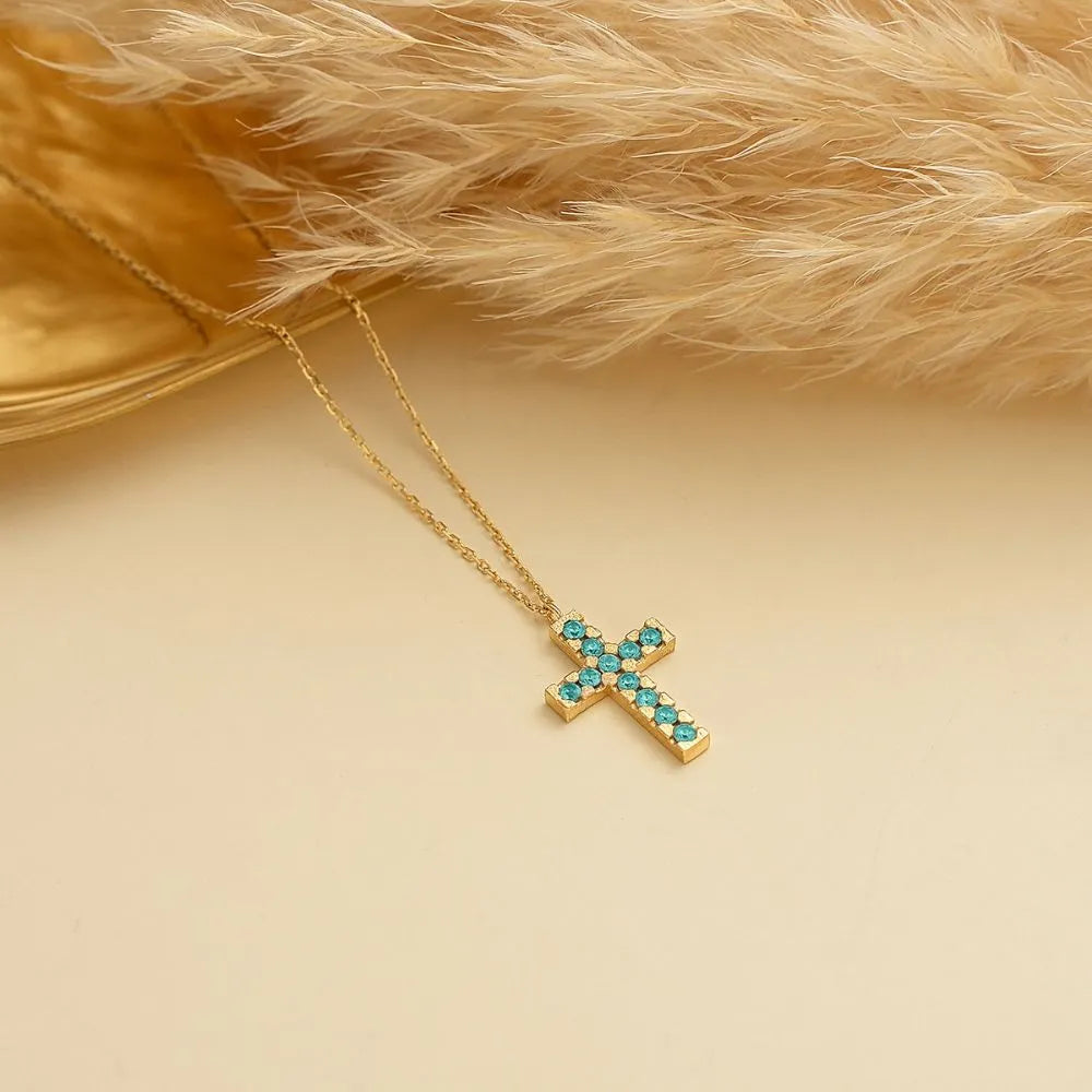 14k Gold cross necklace with turquoise birthstones on a beige background