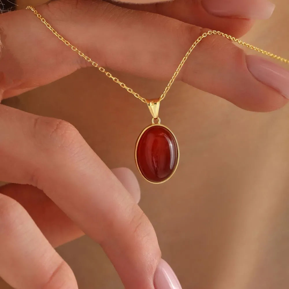 14k Gold necklace with a red Carnelian pendant held by hands against a blurred background