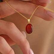 14k Gold necklace with a red Carnelian pendant held by hands against a blurred background