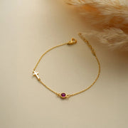 14k Gold cross bracelet with a ruby gemstone on a beige background