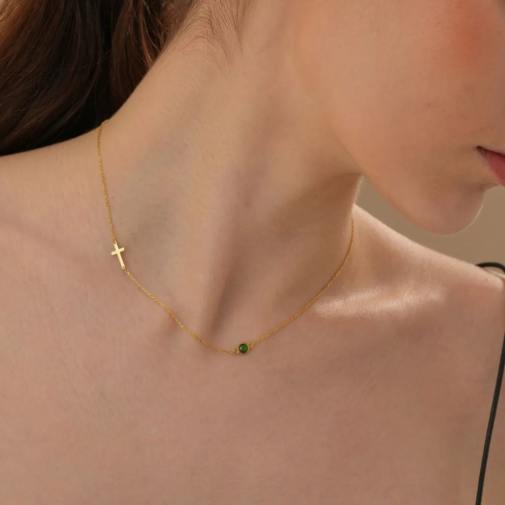 Close-up of a person wearing a 14k gold necklace with a cross pendant and green Emerald gemstone.