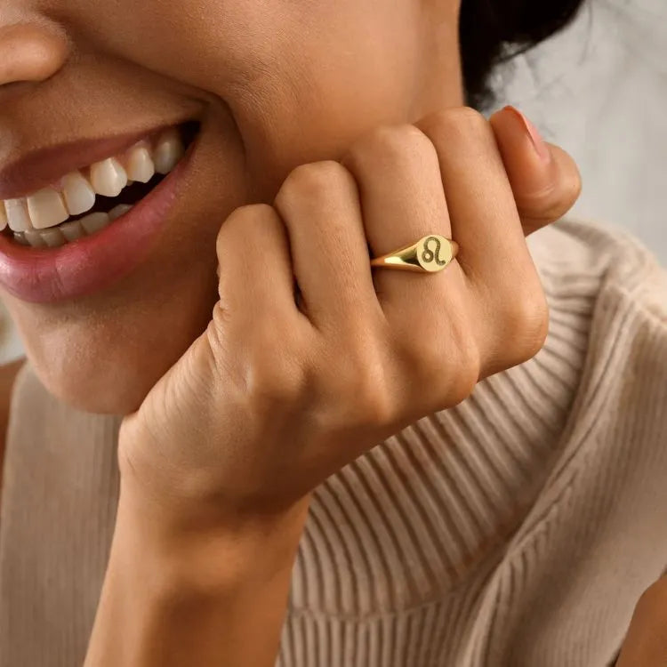 Close-up of a woman model wearing a 14k gold filled signet ring with a leo zodiac symbol on a neutral background