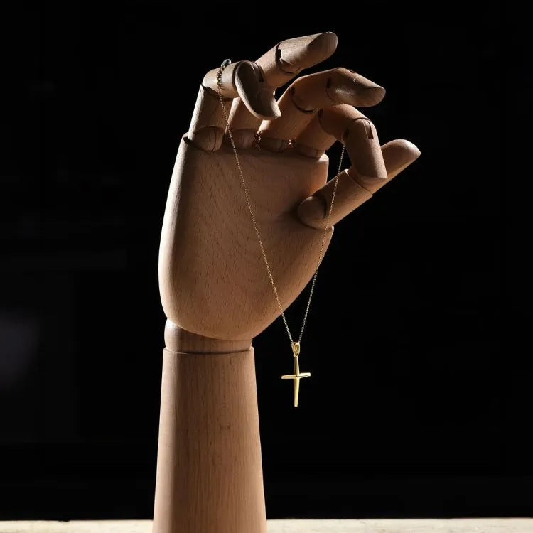 Wooden hand holding a 14k gold filled necklace with a cross pendant against a dark background