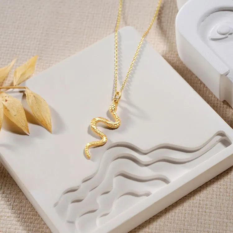 14k Gold filled snake necklace on a decorative white stand with a beige background.