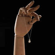 Wooden hand holding a baroque pearl necklace against a black background.
