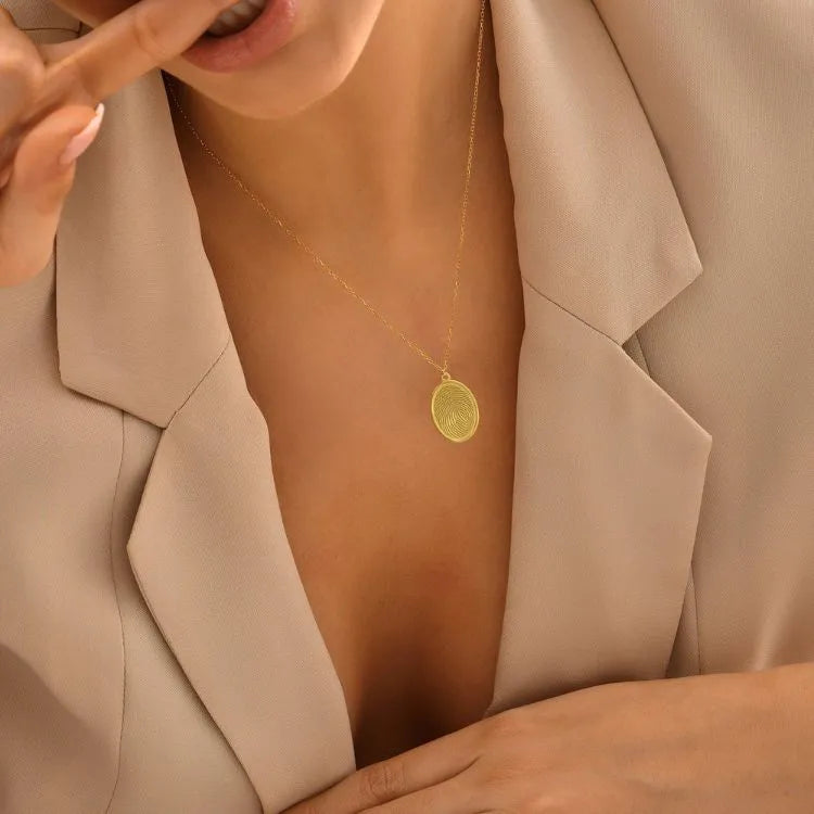 Close-up of a woman model wearing a 14k gold filled fingerprint necklace with anoval pendant, set against a neutral background.