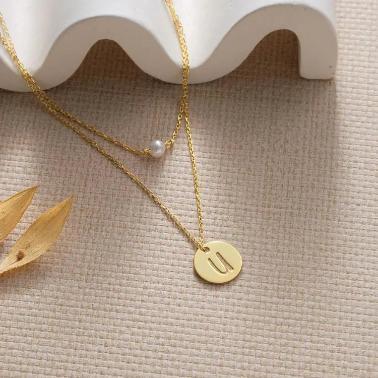 14k gold filled pearl disc layer necklace on a beige surface.