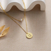 14k gold filled pearl disc layer necklace on a beige surface.