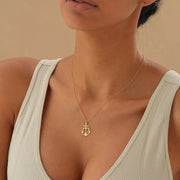 Woman model is wearing 14k Gold necklace with a heart, cross and anchor pendant on a dark surface