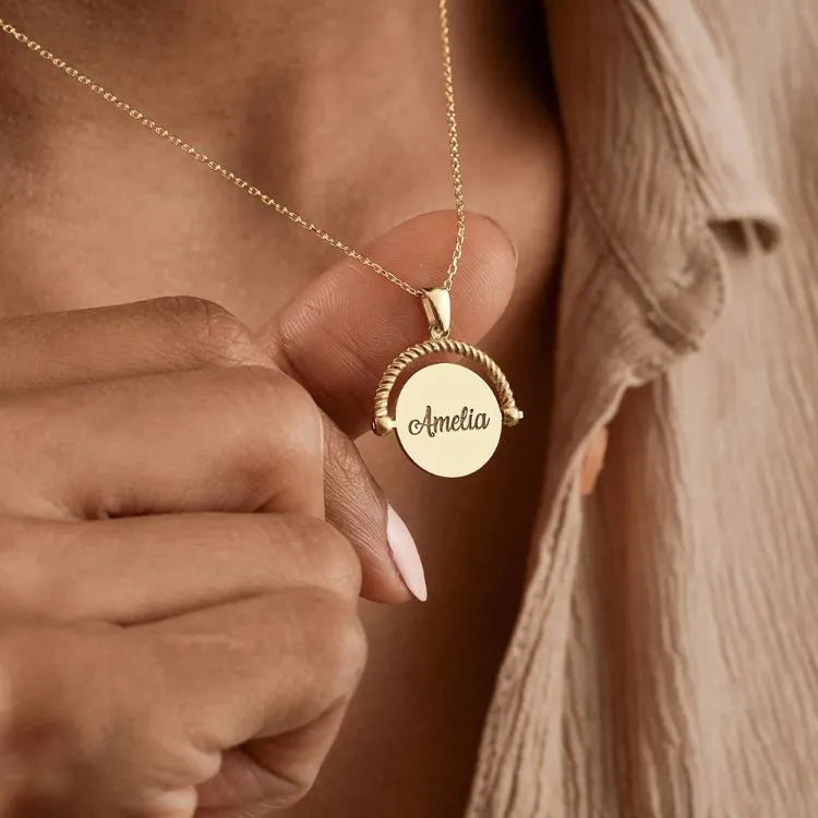 14k Gold filled spinner pendant necklace with a round pendant engraved with 'Amelia' held by a hand.