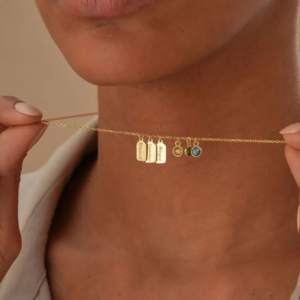 14k Gold necklace with name engraved charms and colorful gemstones held against a neutral background