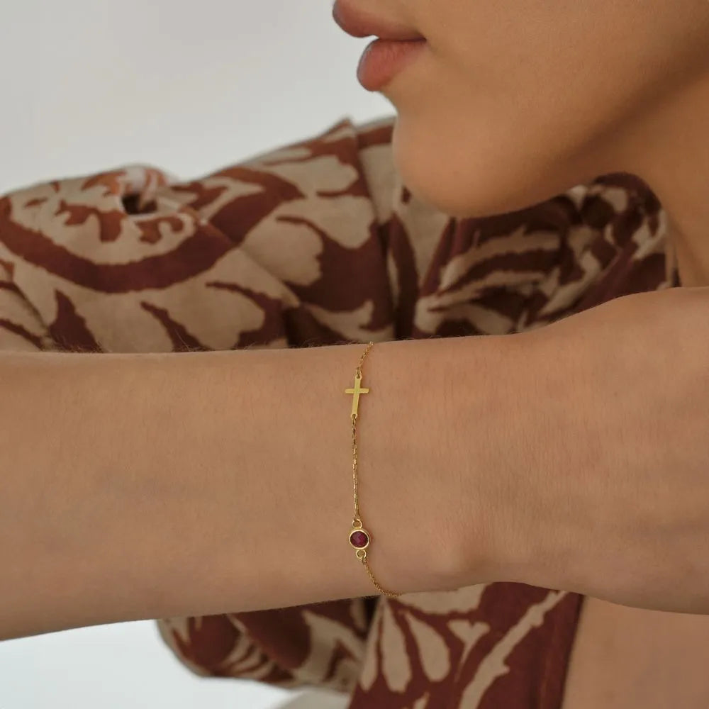 14k Gold bracelet with a red gemstone on a woman model's wrist, wearing a patterned garment.