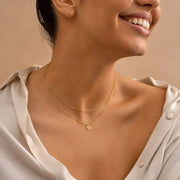 Woman wearing a 14k gold-filled tiny disc layer necklace with a beige background