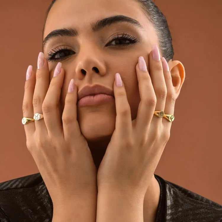 Woman model with 14k gold filled signet rings on her fingers against a brown background