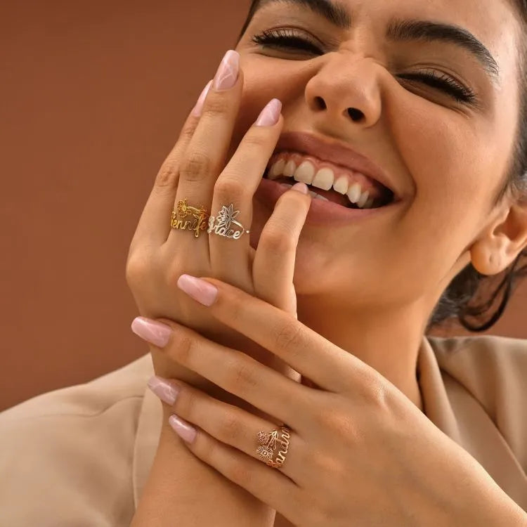Woman model wearing multiple birth flower name rings on her fingers with a warm brown background