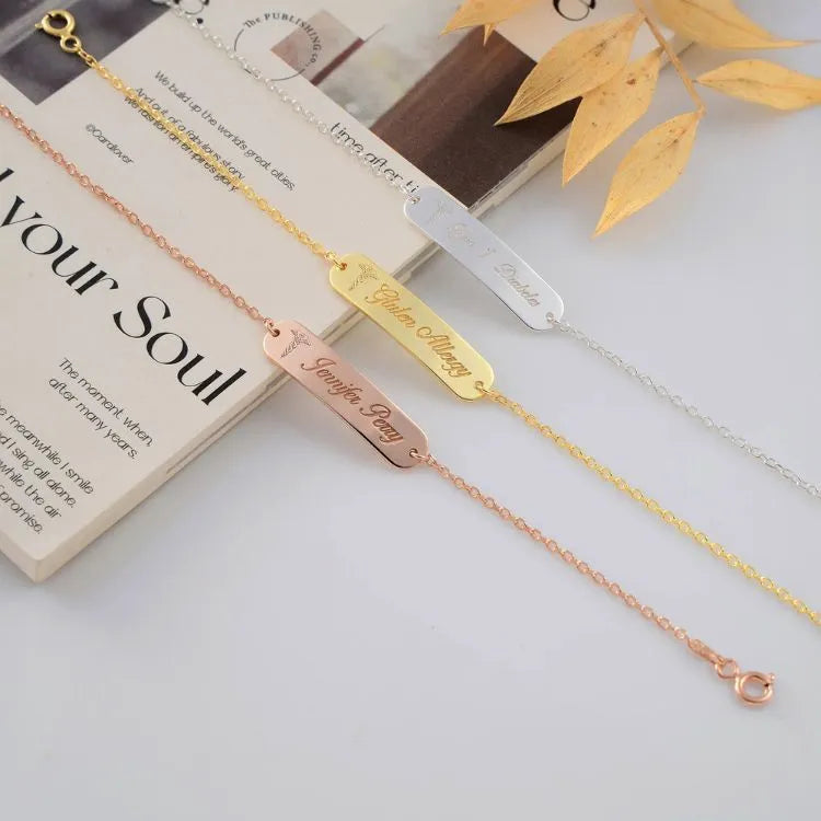 Sterling silver, 14k Gold filled and 14k rose gold filled bracelets with engraved workds on a white surface with a book and leaves in the background.