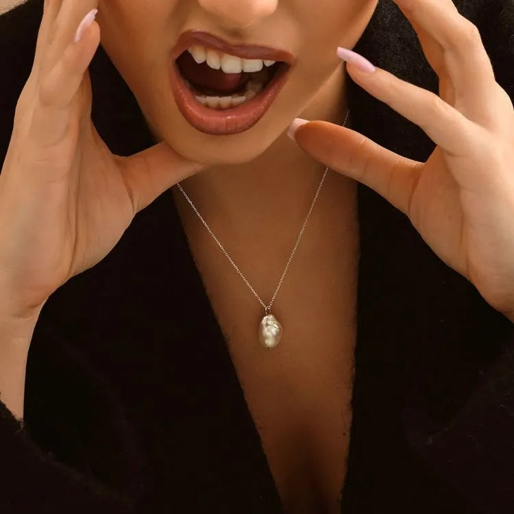 Close-up of a woman model wearing a necklace with a pearl pendant, against a dark background.