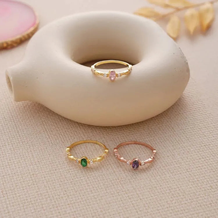 Three 14k gold filled oval birthstone cz diamond rings with gemstones on a textured surface