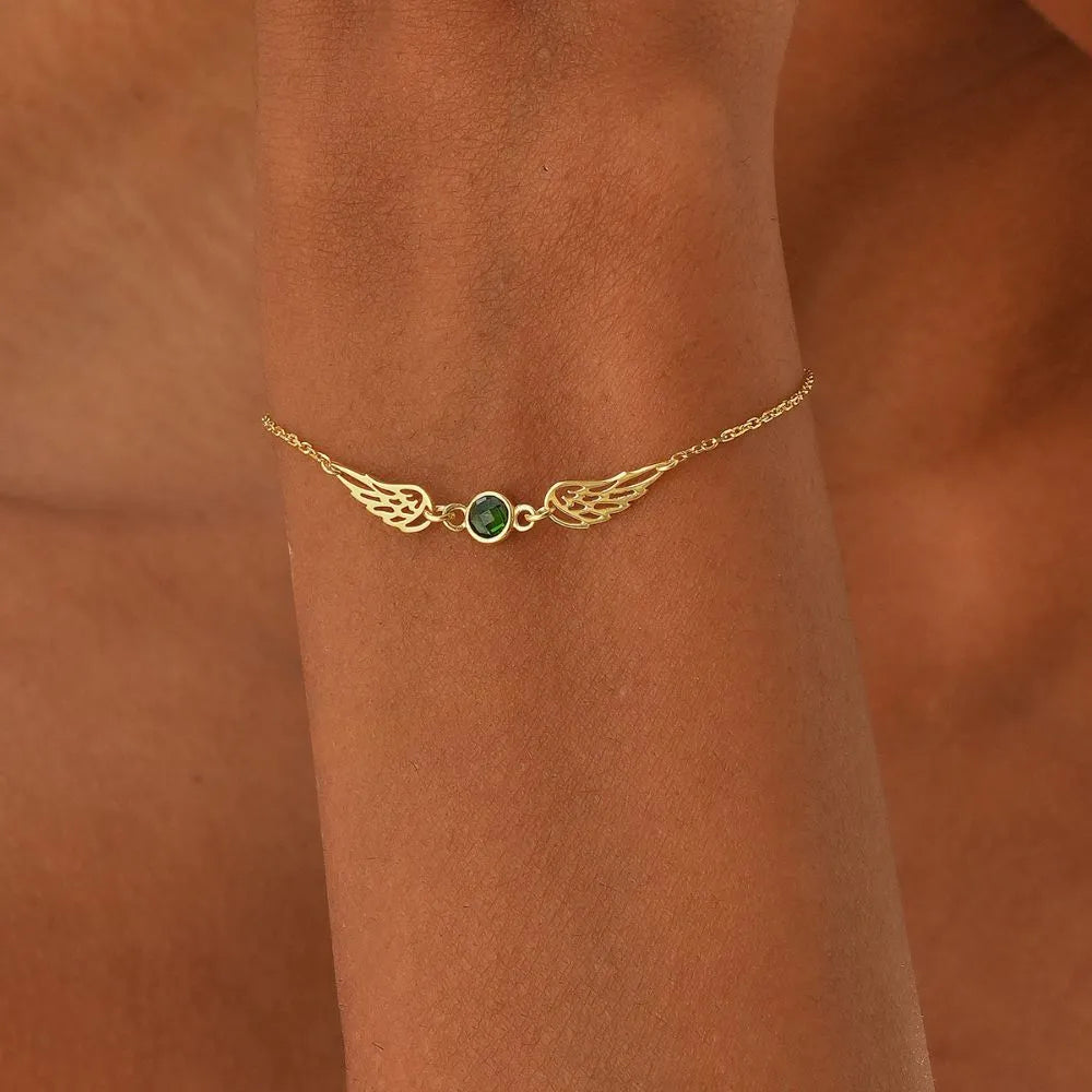 14k Gold bracelet with green Emerald birthstone on a wrist against a brown background