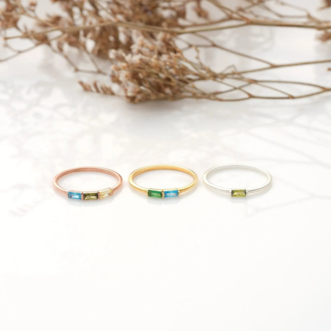 Three baguette birthstone rings in 14k gold-filled, 925 sterling silver, and 14k rose gold-filled with colorful gemstones on a white background.