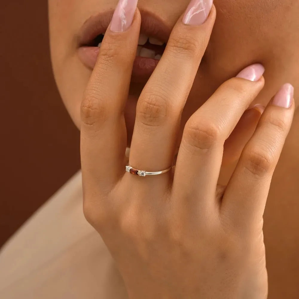 Close-up of a hand with a 925 sterling silver baguette birthstone ring on a brown background.