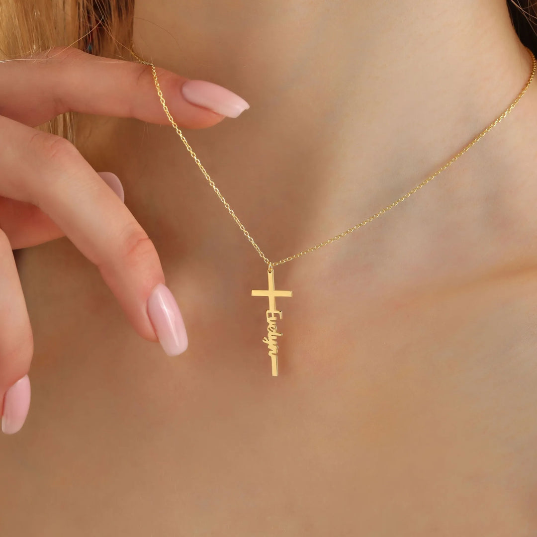 14k Gold name necklace with a cross pendant held by a hand against a neutral background