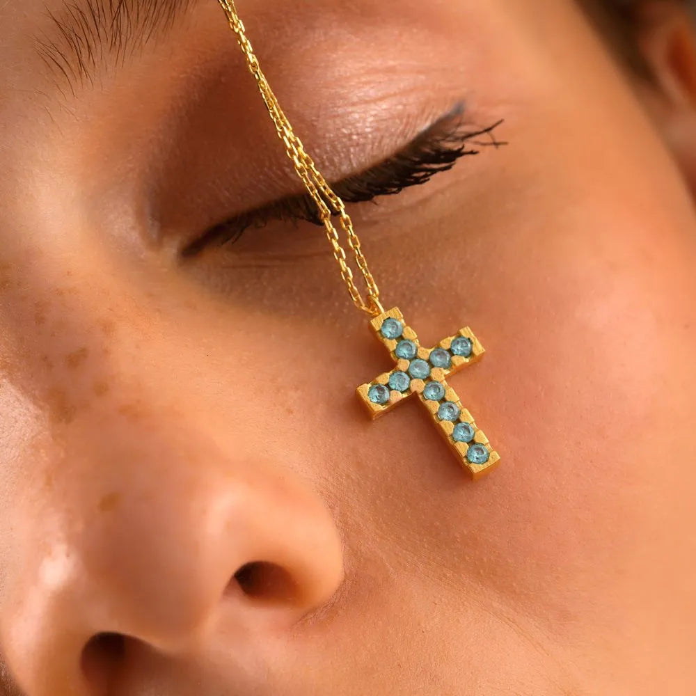 Close-up of a 14k gold cross necklace with gemstones worn by a person.