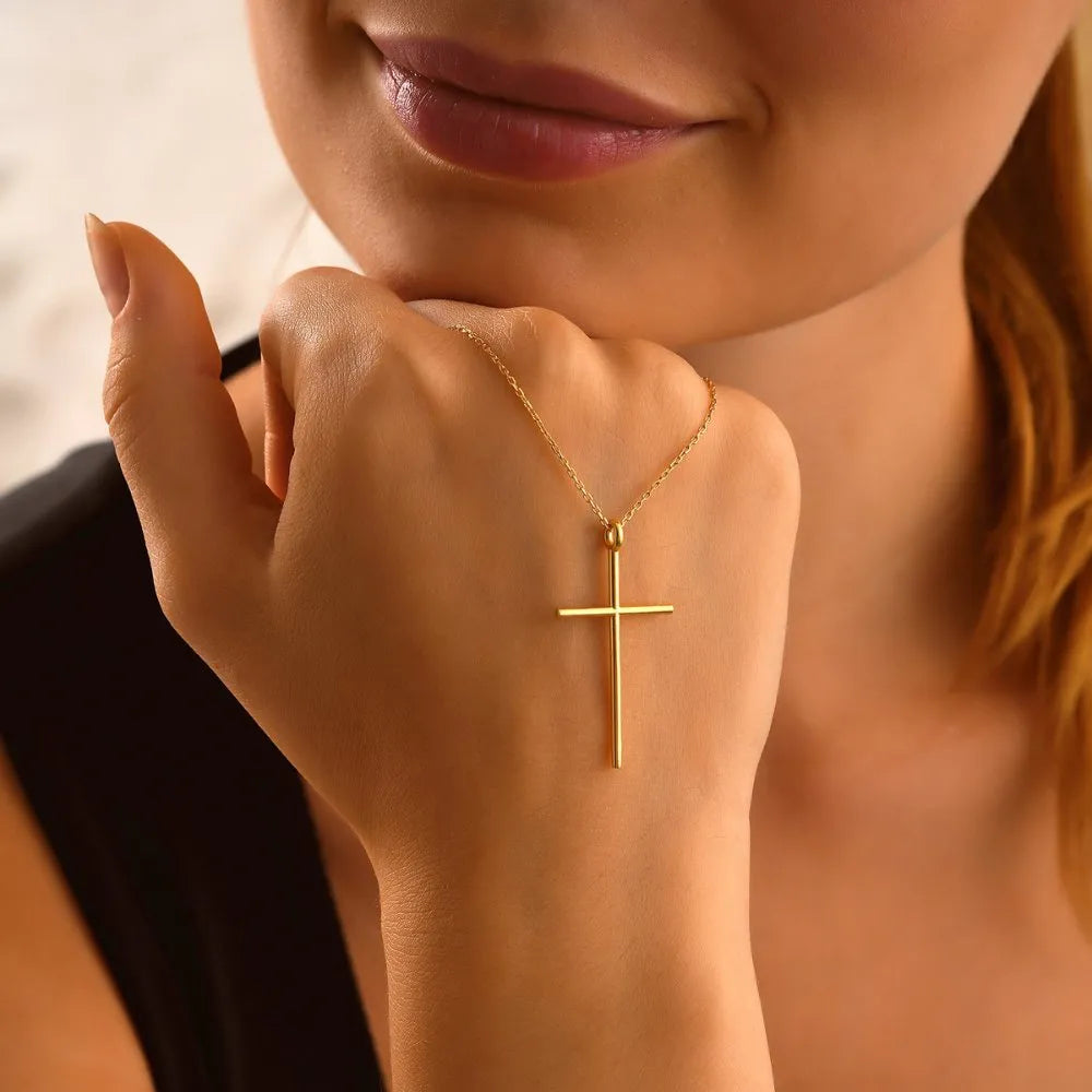 14k Gold cross necklace on a person's wrist with a blurred background