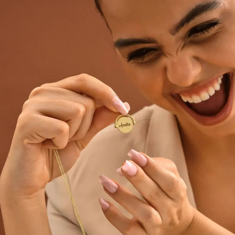 Woman model holding a 14k gold-filled necklace with a pendant, smiling against a warm brown background