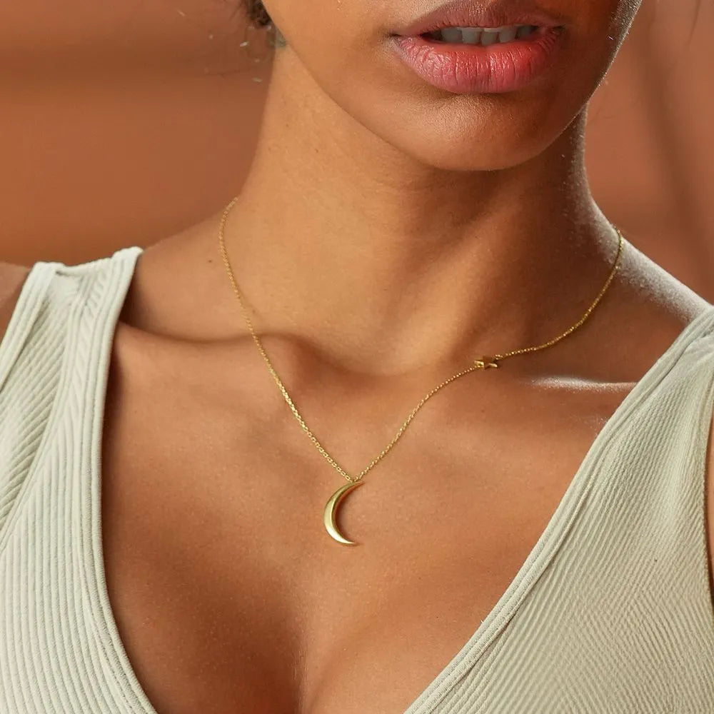 Woman wearing a 14k gold necklace with a crescent moon pendant against a blurred background