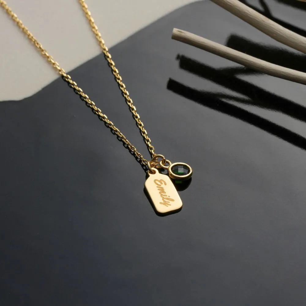 14k Gold necklace with a name engraved tag and birthstone on a dark surface