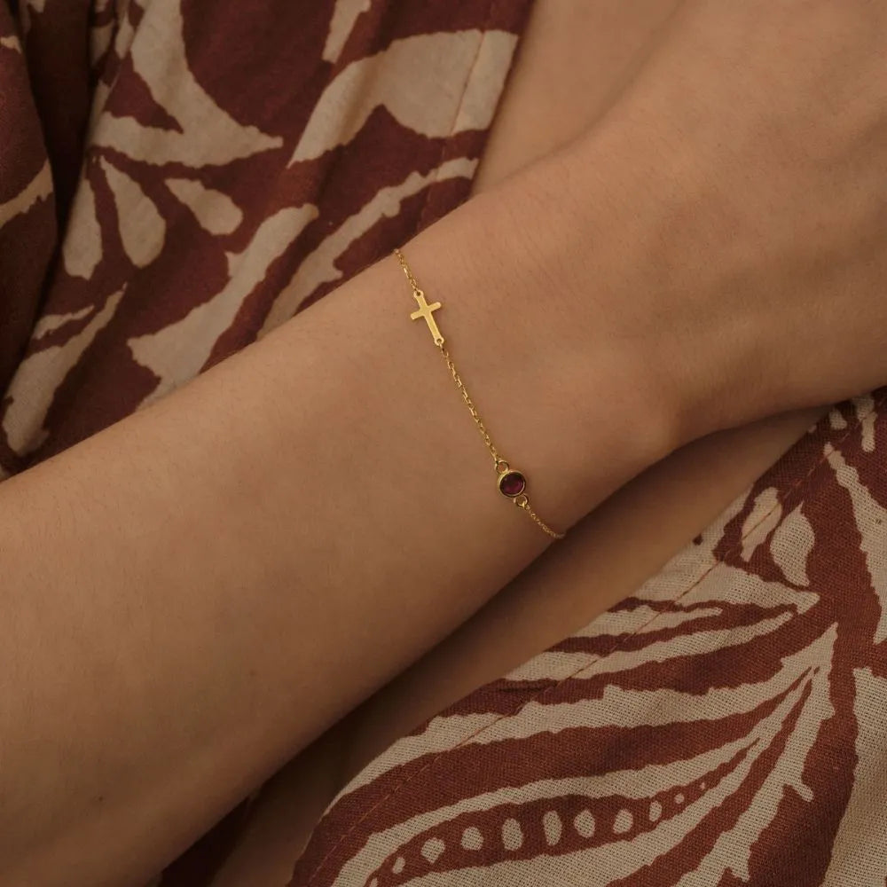 14k Gold bracelet with a red gemstone on a wrist against a patterned fabric background