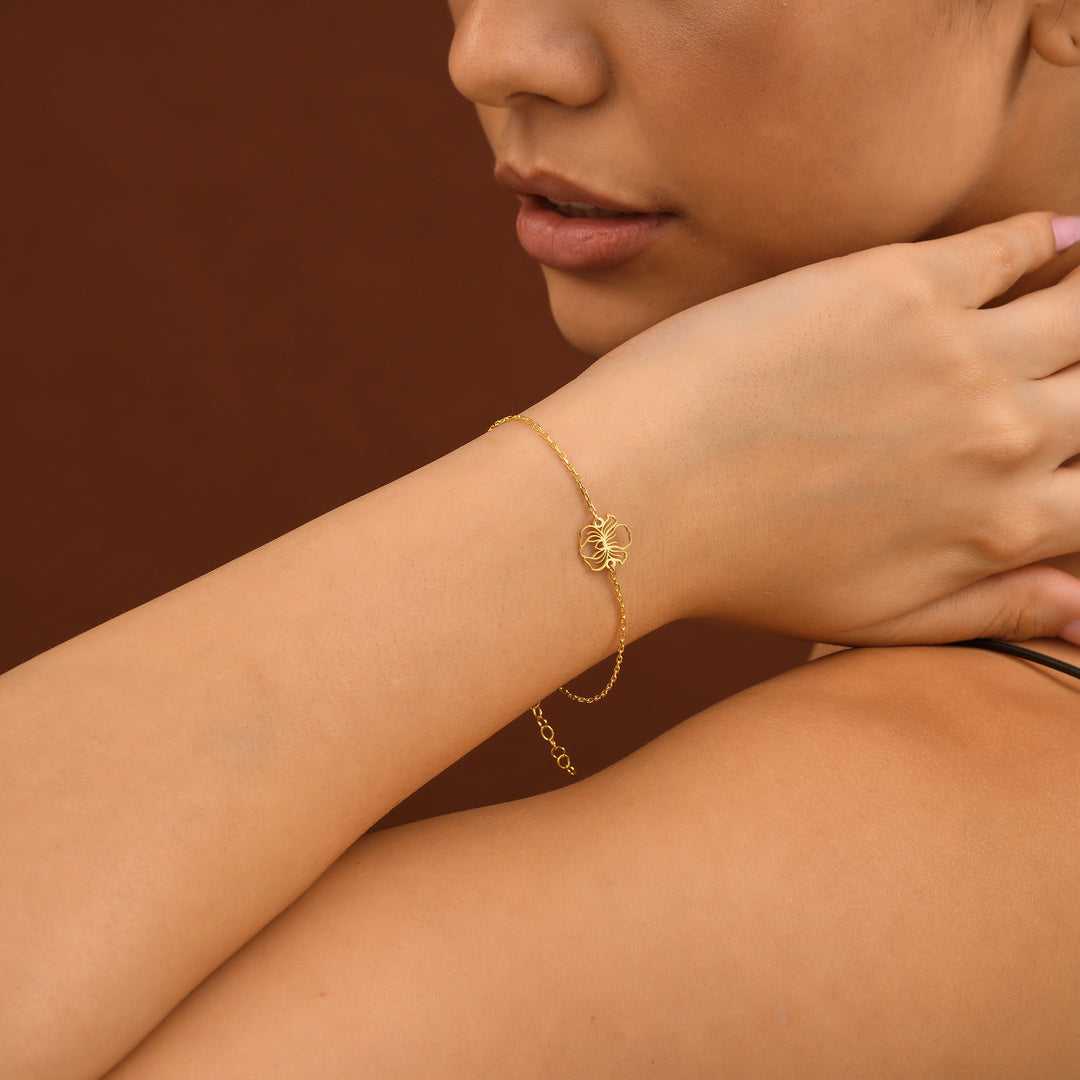 Cut Out Birthflower Bracelet - Close-up of a person wearing a gold bracelet on a brown background