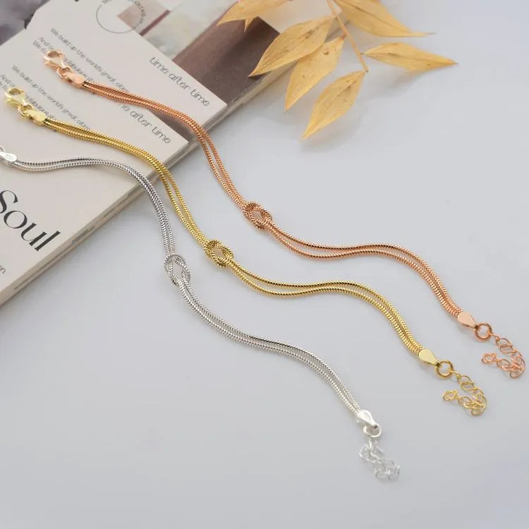 Sterling silver, 14k gold filled, and 14k rose gold filled knot bracelets on a white surface with a magazine underneath.