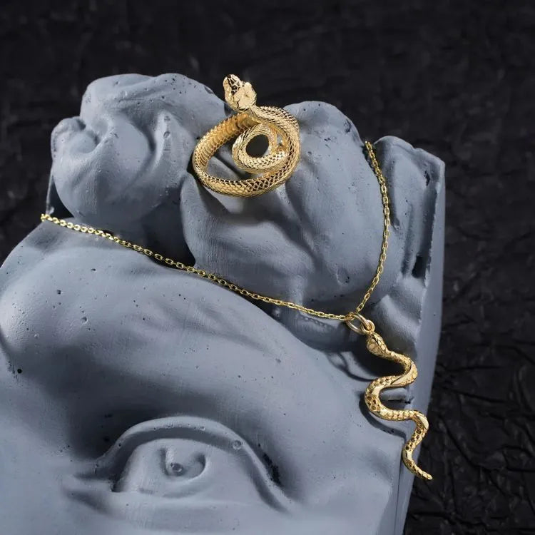 14k Gold filled snake-shaped necklace and ring on a gray stone surface with a dark textured background.