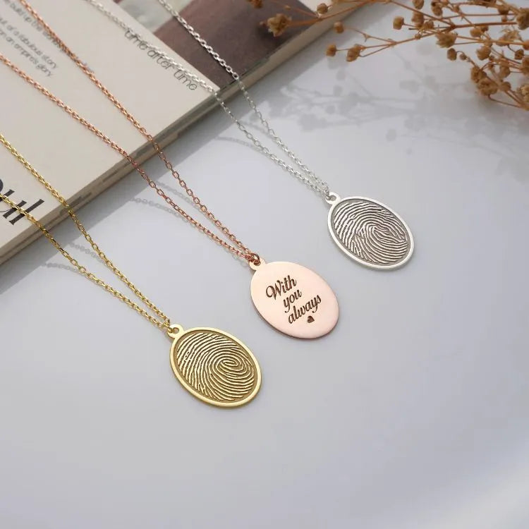 Three fingerprint necklaces on a light surface with a magazine and dried flowers.
Necklace materials:
14k gold filled,
14k rose gold filled,
Sterling silver.