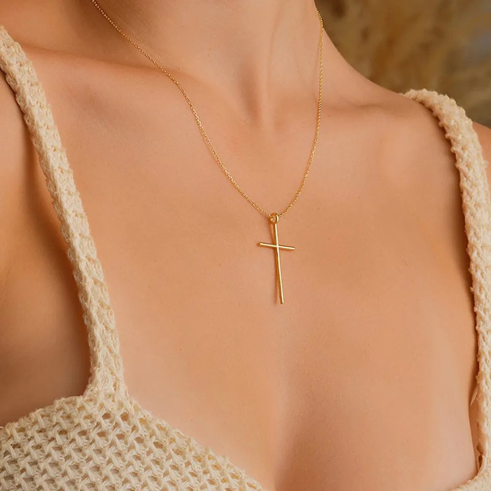 14k Gold cross necklace on a person wearing a beige crochet top with a blurred natural background